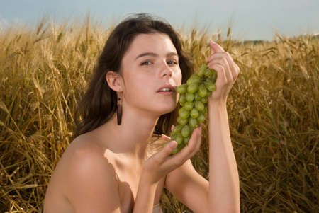 Beautiful slavonic girl on picnic in wheat field with grapesの写真素材