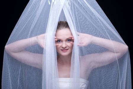 Closeup portrait of beautiful blond girl with blue eyes in white fabric on blackの写真素材