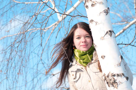 Winter lifestyle. Beautiful girl with green scarf and gloves over birch tree and blue skyの写真素材