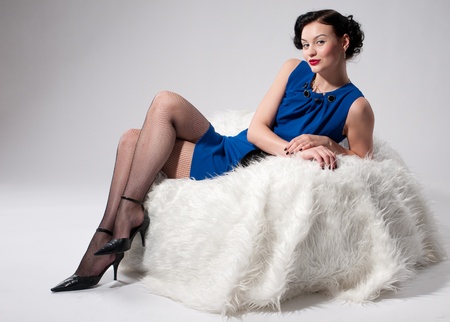 Beautiful glamour woman in blue dress on white fur sofaの写真素材
