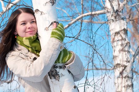 Winter lifestyle. Beautiful girl with green scarf and gloves over birch tree and blue skyの写真素材