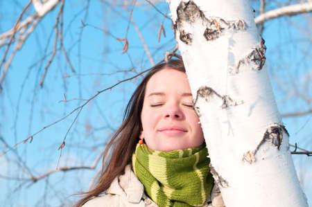 Winter lifestyle. Beautiful girl with green scarf and gloves over birch tree and blue skyの写真素材