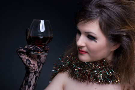 Closeup portrait of beautiful girl in black gloves with red lips, tinsel and wineglass on blackの写真素材