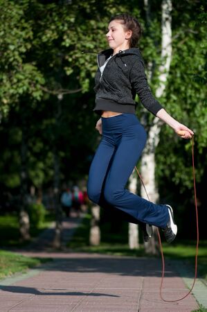 Beautiful young woman doing  exercise with skipping rope at park. Jumping