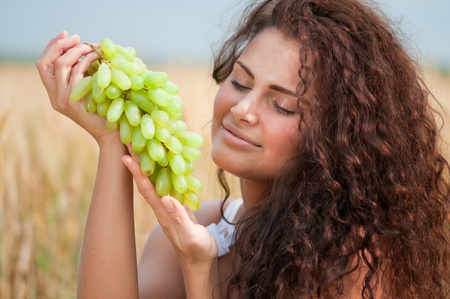 Beautiful woman with perfect hair and skin posing in wheat field and eating green grapes. Picnic.の写真素材