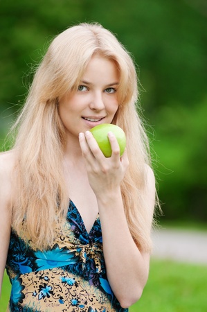 Portrait of a young beautiful woman with green apple at parkの写真素材