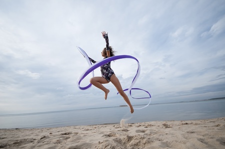 young professional gymnast woman dance with ribbon - outdoor sand beach