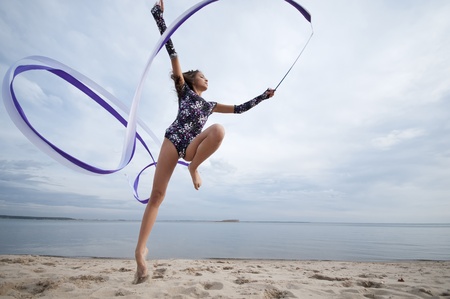 young professional gymnast woman dance with ribbon - outdoor sand beach