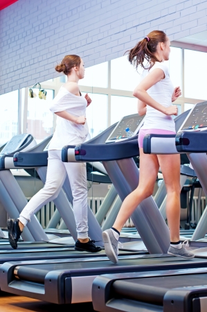 Two young sporty women run on machine in the gym centreの写真素材