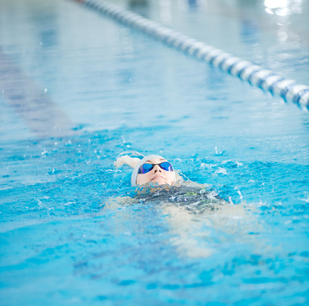 Young woman in goggles and cap swimming back crawl stroke style in the blue water indoor race poolの写真素材