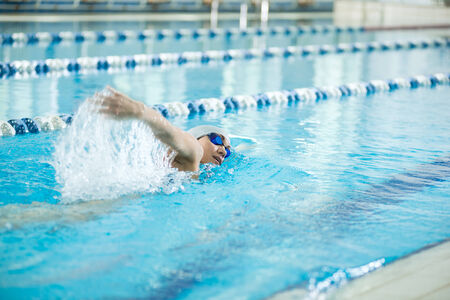 Young woman in goggles and cap swimming front crawl stroke style in the blue water indoor race pool