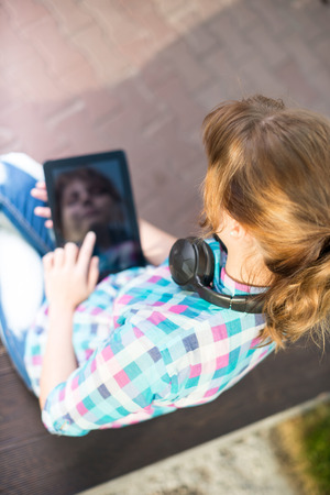 Preparing to exams outdoors. Beautiful young female student writing or reading something from note pad.  Woman sitting on bench in city park.の写真素材
