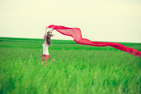 Young lady runing with tissue in green field. Beautiful happy woman walking  in the summer rural meadow. Outdoor summer portrait of pretty sport style woman jumping with fabric. Beautiful fit tan girl. Sexy slim model caucasian ethnicity outdoors.の写真素材