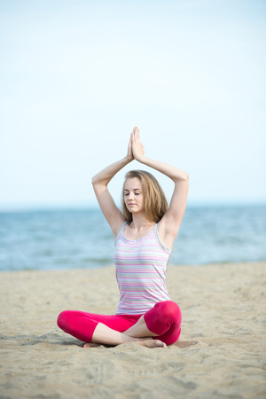 Young lady practicing yoga. Beautiful woman posing at the summer sand beach. Workout near ocean sea coast. Beautiful fit tan girl. Fitness model caucasian ethnicity outdoors. Weight loss exercise. Meditation.の写真素材
