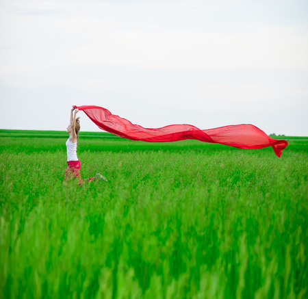 Young lady runing with tissue in green field. Beautiful happy woman walking  in the summer rural meadow. Outdoor summer portrait of pretty sport style woman jumping with fabric. Beautiful fit tan girl. Sexy slim model caucasian ethnicity outdoors.の写真素材