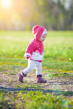 Happy little girl walking in the meadow and looking at the sun. Green field.の写真素材