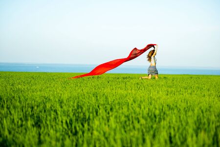 Young lady runing with tissue in green field. Beautiful happy woman walking in the summer rural meadow. Beautiful fit tan girl. Sexy slim model caucasian ethnicity outdoors.の写真素材