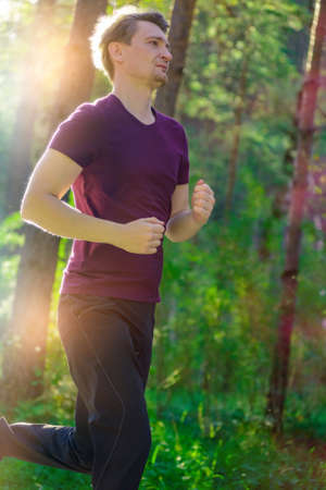 Running man jogging in city park at beautiful summer day. Sport fitness model caucasian ethnicity training outdoor.の写真素材