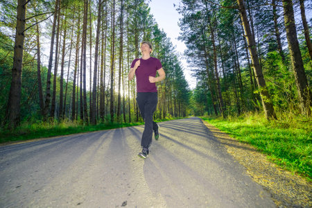 Running man jogging in city park at beautiful summer day. Sport fitness model caucasian ethnicity training outdoor.の写真素材