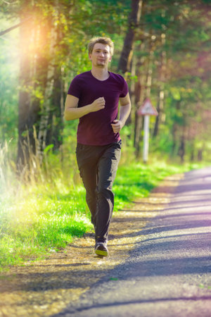 Running man jogging in city park at beautiful summer day. Sport fitness model caucasian ethnicity training outdoor.の写真素材
