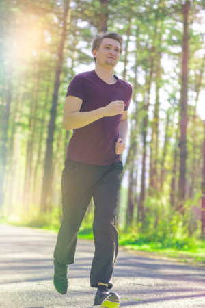 Running man jogging in city park at beautiful summer day. Sport fitness model caucasian ethnicity training outdoor.の写真素材
