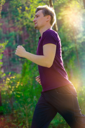 Running man jogging in city park at beautiful summer day. Sport fitness model caucasian ethnicity training outdoor.の写真素材