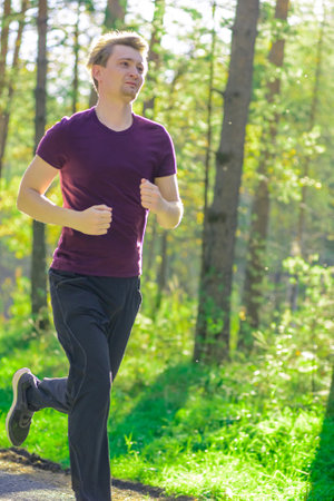 Running man jogging in city park at beautiful summer day. Sport fitness model caucasian ethnicity training outdoor.の写真素材