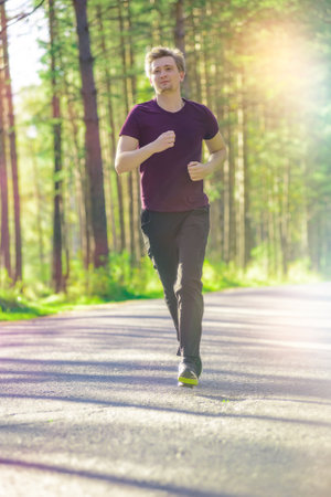 Running man jogging in city park at beautiful summer day. Sport fitness model caucasian ethnicity training outdoor.の写真素材