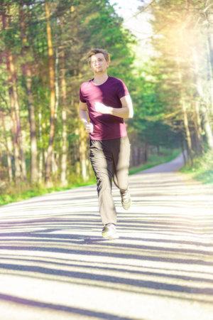 Running man jogging in city park at beautiful summer day. Sport fitness model caucasian ethnicity training outdoor.の写真素材