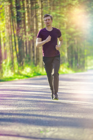 Running man jogging in city park at beautiful summer day. Sport fitness model caucasian ethnicity training outdoor.の写真素材
