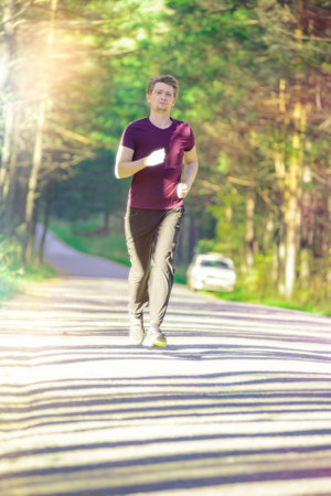 Running man jogging in city park at beautiful summer day. Sport fitness model caucasian ethnicity training outdoor.の写真素材
