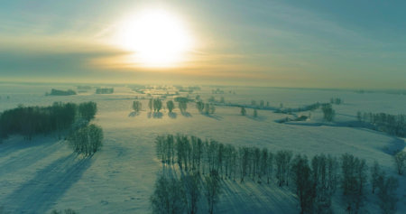 Drone aerial view of cold winter landscape arctic field, trees covered with frost snow, ice river and sun rays over horizon. Extreme low temperature weather.の写真素材