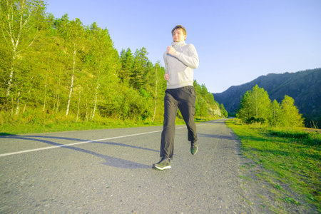 Running man jogging in city park at beautiful summer day. Caucasian ethnicity training outdoor.