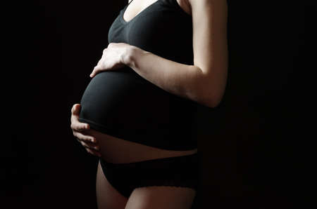 midsection of pregnant woman in black clothes on a black backgroundの写真素材