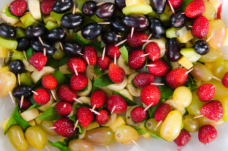 kiwi, banana, strawberries, grapes, cheese impaled on skewers on a plateの写真素材