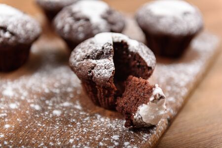 chocolate muffins with white icing lying on a Board sprinkled with powdered sugar