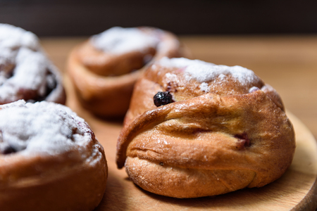 bun with currants covered with powdered sugar lay on a chopping board brownの写真素材