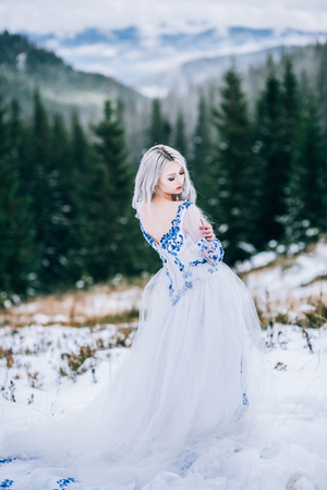 groom in a blue suit and bride in white, embroidered with blue pattern, dress on a background of green pine forests in the mountains of the Carpathiansの写真素材