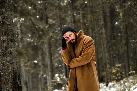 man in the winter forest is cold and in a brown coat and glovesの写真素材