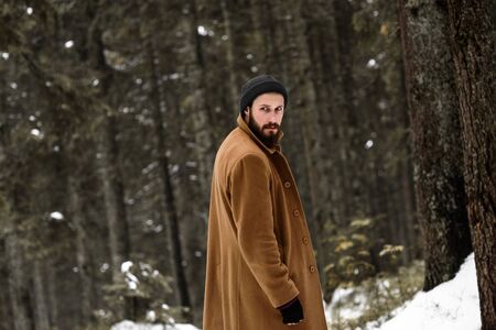 man in the winter forest is cold and in a brown coat and glovesの写真素材