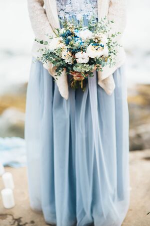 the bride's bouquet in hands of the girl who stands on the rocks in a gray dressの写真素材