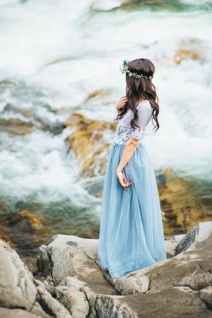 the bride looks to the moan of the stream of the mountain river, standing on a rockの写真素材