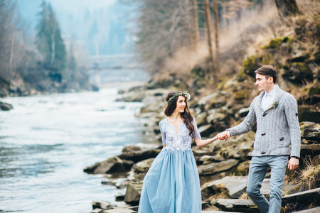 the bride and groom walking on the shore of a mountain riverの写真素材
