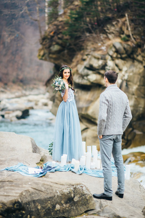 the bride is facing the groom with a bouquet on the background of a waterfallの写真素材