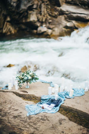 wedding decor with a bouquet and candles on the stones of the Carpathian waterfallの写真素材