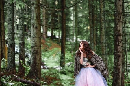 the bride wanders alone in the woods in a fur Cape and white dressの写真素材