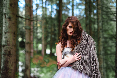 the bride wanders alone in the woods in a fur Cape and white dressの写真素材