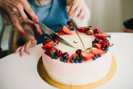 cutting baby cake with strawberries and blueberries mom and daughterの写真素材