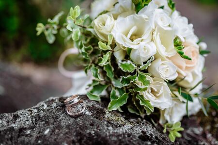 wedding rings on the stone next to the bride's bouquetの写真素材