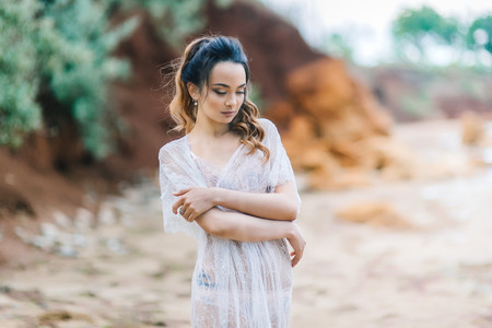 bride in her underwear and a dressing gown with a veil walks on the beachの写真素材
